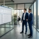 Zwei Berater prüfen im Glasbüro die ILM-Objektliste aus SAP-Hinweis 2122906 vor einem Bildschirm mit Unternehmenssoftware (KI-generiertes Bild)