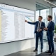 Zwei Berater besprechen die Archivierung von Spool-Listen in SAP HCM vor einem SAP-GUI-Screen im Glasbüro (KI-generiertes Bild)